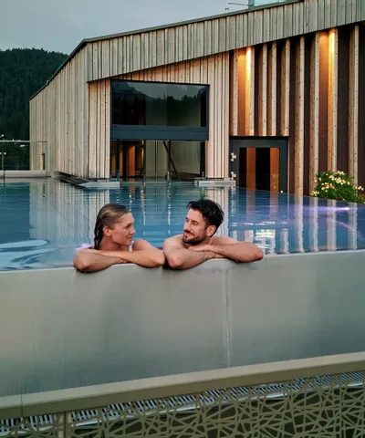 Paar entspannt im Infinity-Pool auf dem Dach eines luxuriösen Alpinresorts mit Holzarchitektur